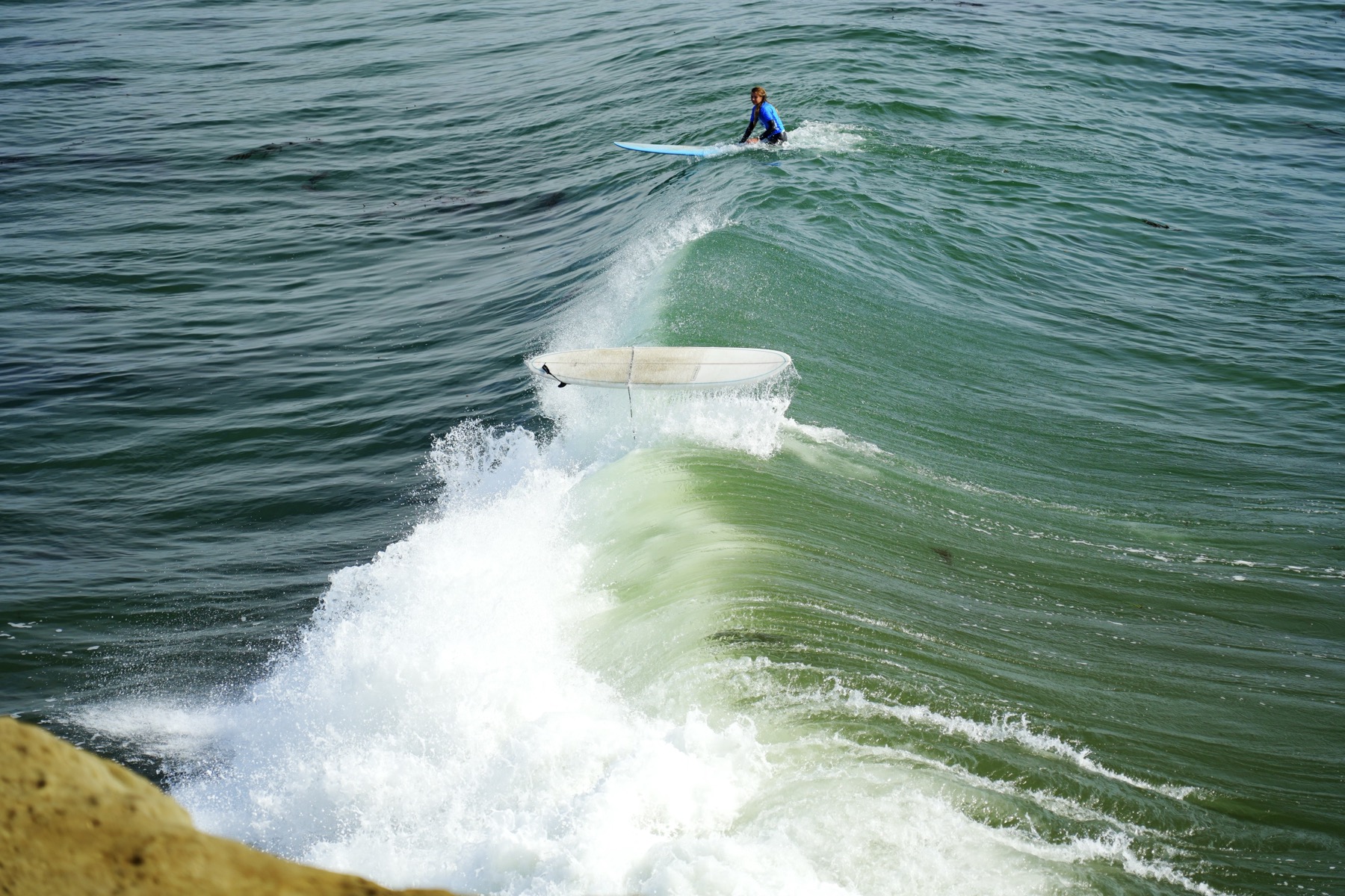 An unoccuppied surf board is suspended in mid-air backwards above a crashing wave.