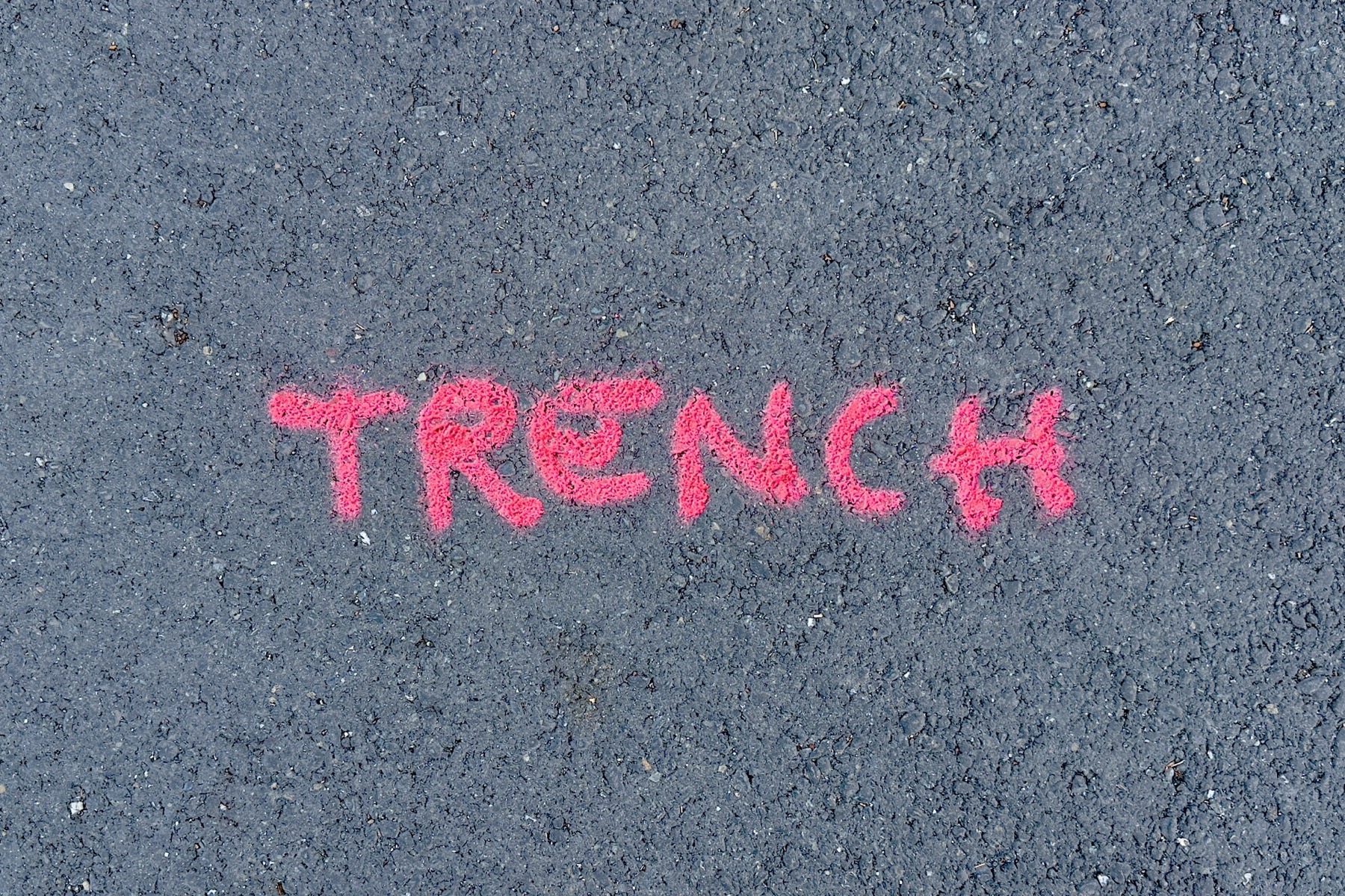 A paver's graffiti of the word 'trench' on a canvas of black asphalt.