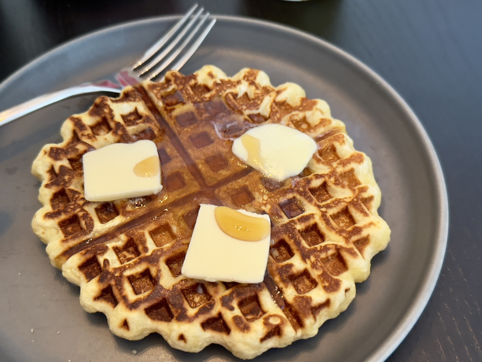 A round waffle on a plate. There are three, yes three, pats of butter. And maple syrup.