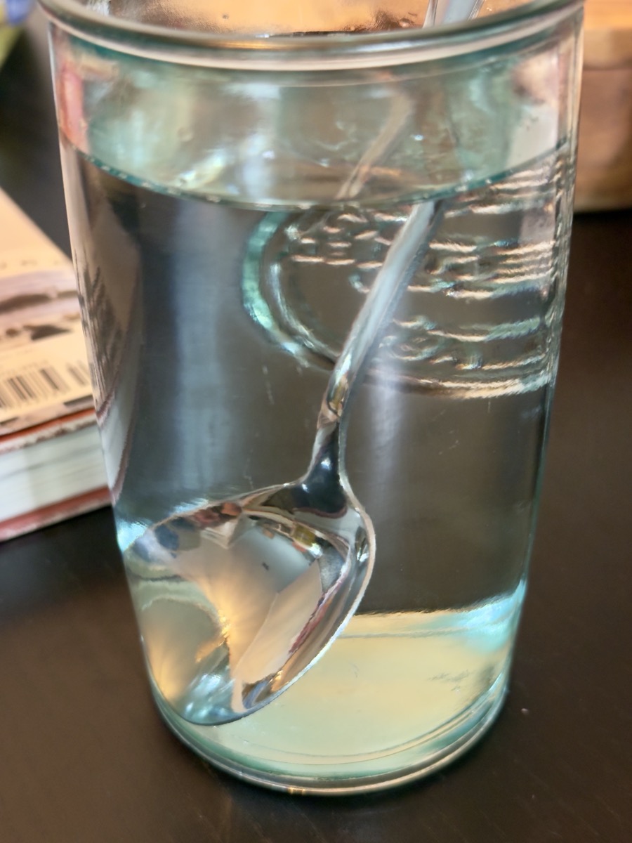 A spoon in a glass filled with water. The glass and water optically distort the spoon.