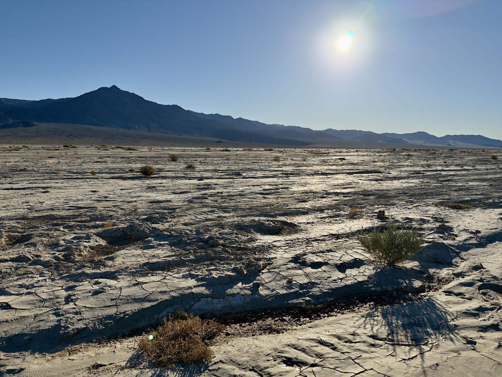 Dry riverbed and bright sun, silhouetted mountains in the distance.